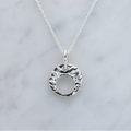 A silver pendant necklace with a textured, hammered circular disc design on a delicate link chain, displayed on a light gray marble surface. A small 'Made with AI' label is in the top right corner.